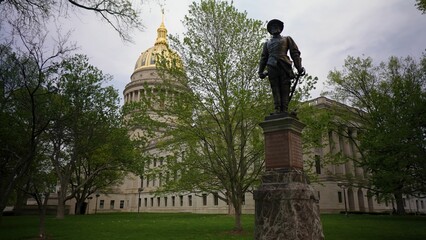 Visitors admire the West Virginia State Capitol in Charleston, featuring its impressive architecture and a notable statue, surrounded by lush greenery and trees.