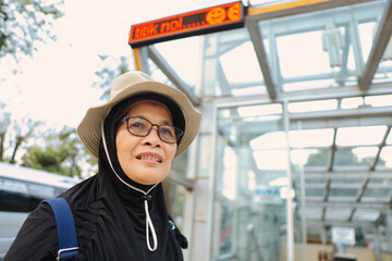 Woman in Glasses Smiling at Bus Stop Under Sunny Skies