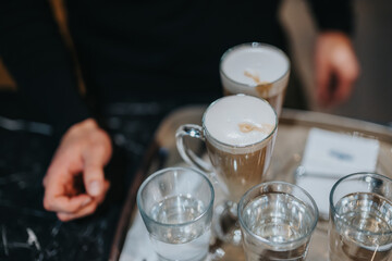 A tray holding multiple glasses of coffee and water in a cozy cafe atmosphere. The image highlights...