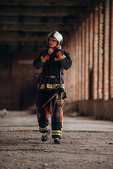 Fototapeta premium Wearing the helmet. Firefighter in professional equipment is indoors in abandoned building
