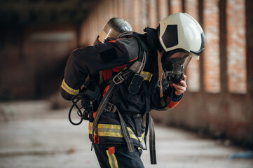 In mask, preparing air balloon. Firefighter in professional equipment is indoors in abandoned...