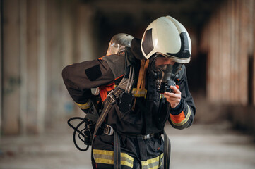 In mask, preparing air balloon. Firefighter in professional equipment is indoors in abandoned...