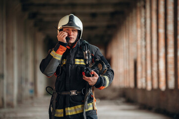 With walkie talkie radio. Firefighter in professional equipment is indoors in abandoned building