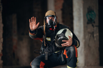 Stop hand gesture. Firefighter in professional equipment is indoors in abandoned building