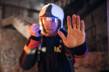 No trespassing, stop hand gesture. Firefighter in professional equipment is indoors in abandoned...