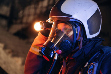 Side view, looking for the way with flashlight. Firefighter in professional equipment is indoors in...