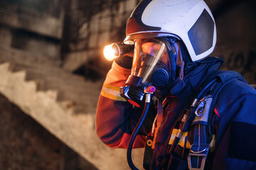 Side view, looking for the way with flashlight. Firefighter in professional equipment is indoors in...