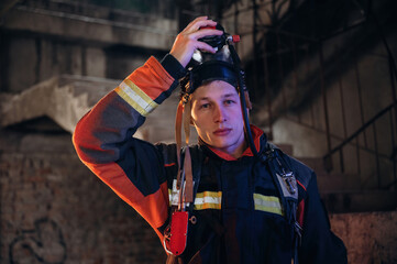 Against old stairs. Firefighter in professional equipment is indoors in abandoned building