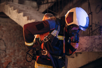 Adjusting air flow into the mask. Firefighter in professional equipment is indoors in abandoned...