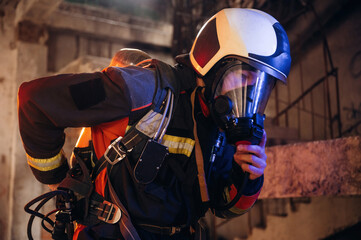 Hard to breathe, using air mask. Firefighter in professional equipment is indoors in abandoned...