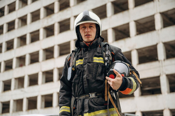 Many of the windows behind him. Professional firefighter is standing outdoors against big...
