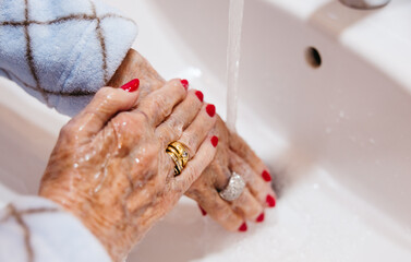 Close-up of senior woman rinsing hands under running tap water