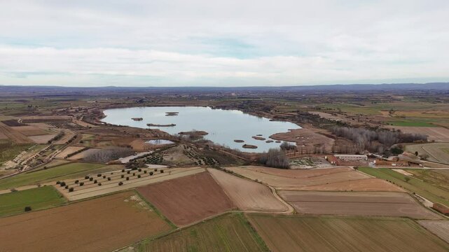 Aerial perspective of a large lake bordered by agricultural fields and patches of woodland, showcasing the serene rural landscape under a slightly overcast sky.