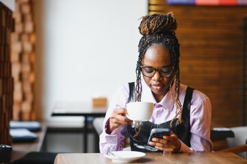 Young african woman at cafe drinking coffee and using mobile phone