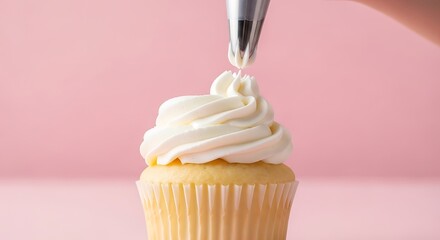 Close up of a hand piping white frosting onto a vanilla cupcake on pink background icing cream