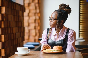 African woman with afro hair eating a tasty classic burger with fries. Cheat Meal