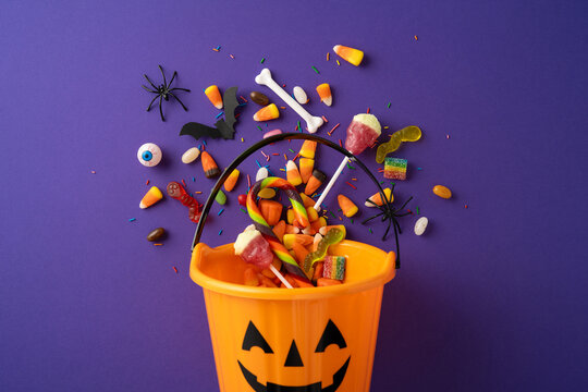 Bright yellow pumpkin bucket filled with Halloween candies surrounded by festive decorations