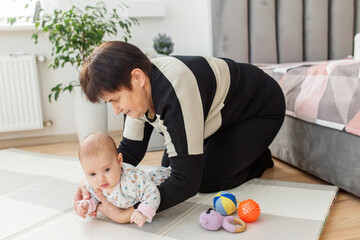 Grandmother helping baby during tummy time on play mat. Baby care.