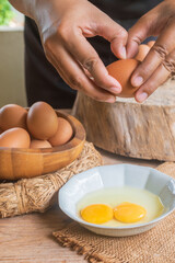 A detail of cracked egg falling into the pan as woman holds egg shells in both hands.