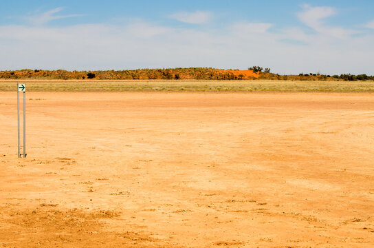 Direction arrow on a desert claypan with red sand dunes in the distance