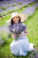 Beautiful brunette young woman In white dress and straw hat  relaxing ad holding lavender bouquet...