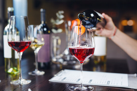 Faceless sommelier pours red wine into stem glass.
