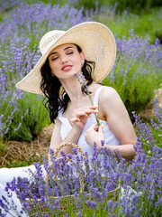 Beautiful brunette young woman In white dress and straw hat  sitting with straw basket  in lavender...