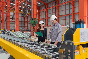 Two worker with safety helmet and black suit standing in a factory, holding clipboard, used for taking note, check schedule and review document.