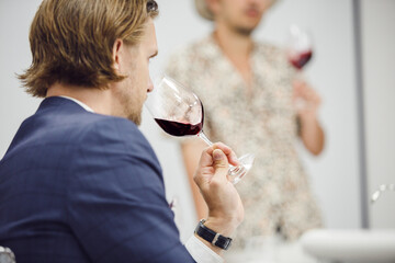Good looking caucasian ethnicity man tasting red wine from glass being trained as sommelier at...