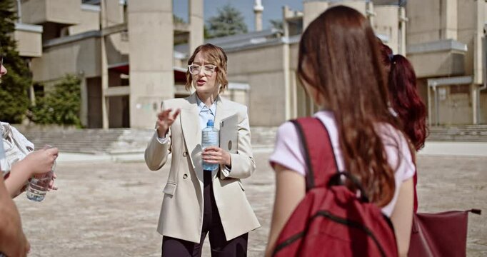 A captivating female teacher enthusiastically guides a diverse group of university students during an outdoor discussion on campus. This scene represents collaborative learning, and mentorship.