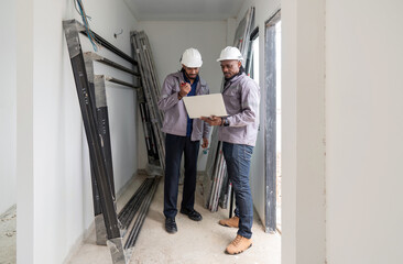 Two construction manager examine plan inside a developing project site. Various construction material surround them, indicating ongoing work. The early morning light create a focused atmosphere.