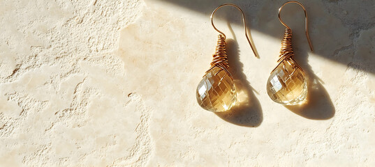 Shimmering drop earrings placed on rustic light stone under warm sunlight creating soft shadows and highlighting intricate wire wrapping and subtle crystal details

