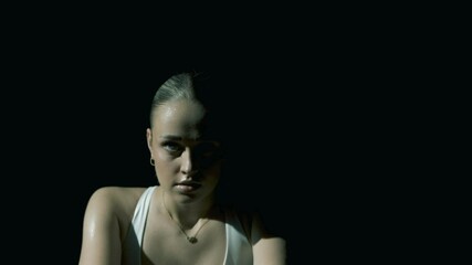 Tight frontal closeup on a woman’s eyes as the camera slowly pulls back, revealing her full face and shoulders while she trains, framed in soft cinematic lighting with a dark, moody background