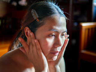 Beauty & Skincare, Asian woman applies facial cream sitting near a sunlit window She massaged her...