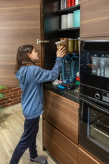 Girl adding container of peanuts to 72 hours survival kit stored in cupboard. Female preparing...