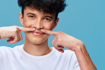young man making a mustache gesture with his fingers on blue background, playful expression, casual...