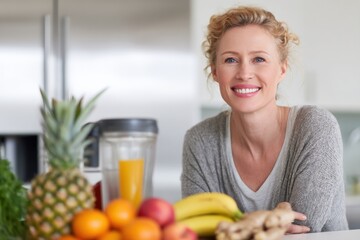 Bright smiling woman sitting at kitchen counter with fresh fruits pine bananas ginger and orange juice in a modern home interior