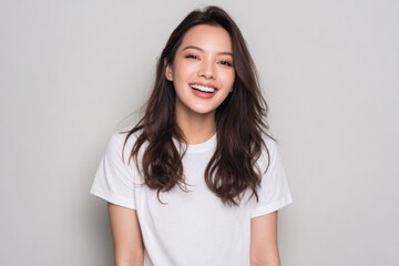 Fototapeta premium Happy Young Woman Smiling Brightly Showing White Teeth Wea Casual White T-Shirt with Long Wavy Hair Isolated on Light Gray Background