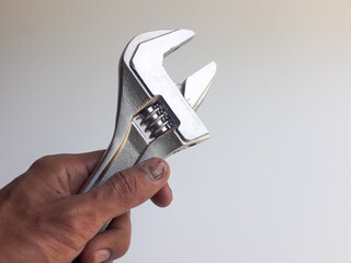A man's hand holding a wrench, also known as an adjustable wrench, is shown on a white background. This wrench is a multi-purpose tool designed to tighten or loosen bolts or nuts with adjustable jaws.