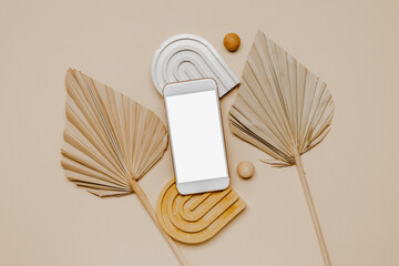 Smartphone with white mockup screen and palm leaves with aesthetic decorative elements top view, brown and beige tone. Smartphone with copy space for branding, website promotion and design
