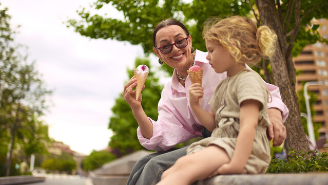 Hug and scoop. Grandmother and granddaughter enjoy ice cream cones on bench. Concept of everyday sweetness, intergenerational love, and peaceful leisure time. - Powered by Adobe