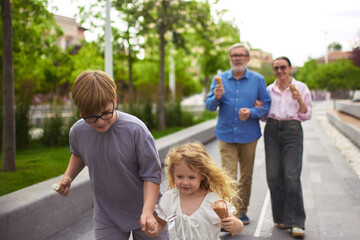Slow and sweet. Family delighting in a sunny walk outside together. Concept of urban relaxation, multigenerational bonding, childhood energy, and weekend tradition with nature and dessert.