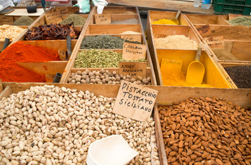 Colorful display of various spices and nuts in wooden boxes at a vibrant market with labels and scoops