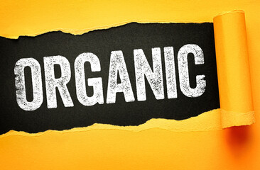 ORGANIC written in bold, distressed white font on a black background revealed through torn yellow paper. Concept for natural, eco-friendly, sustainable, or health-conscious messaging