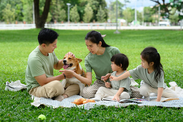 A joyful family shares laughter, snacks, and dog cuddles on a sunny green law
