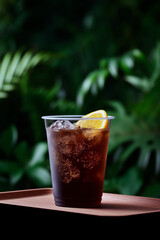 Iced coffee in plastic cup with orange slice near window during sunset with nature view