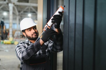 Indian worker is applying polyurethane foam to fill gap between sash and window frame in...