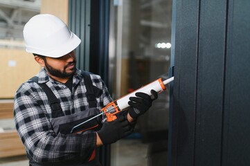 Indian worker is applying polyurethane foam to fill gap between sash and window frame in...
