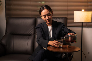 Businesswoman holding a glass of whiskey, sitting and drinking in a room