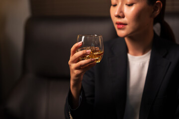 Businesswoman holding a glass of whiskey, sitting and drinking in a room